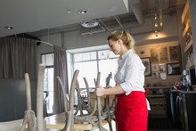 Waitress Placing Chairs On Table In Bistro