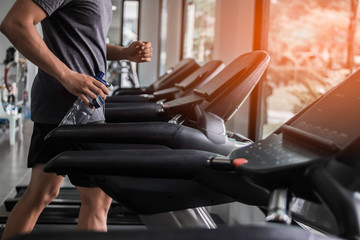 Man is jogging on treadmill with holding bottle water at gym.