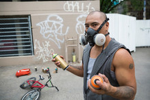 Portrait Graffiti Artist Wearing Protective Mask With Spray Paint In Urban Alley