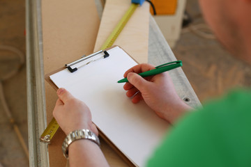 Arms of worker making notes on clipboard with green pen closeup. Manual job DIY inspiration improvement fix shop graphic joinery startup workplace idea designer career wooden bar ruler