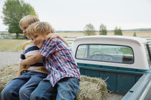 Playful Boys Embracing On Back Of Pick-up Truck At Farm