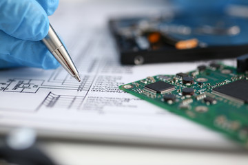 Wall Mural - The male hand of the repairman holds a pen, compares the electronic schematic with the details of the printed circuit board