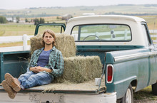 Man Relaxing Against Hay Bales In Back Of Pick-up Truck