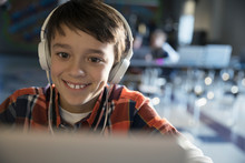 Close Up Smiling Pre-adolescent Boy Wearing Headphones Listening To Music At Laptop
