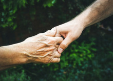 Senior And Young Hands Outside Closeup. Elderly Woman And Young Man Holding Hands Together, Green Blurred Background, Sunlight. Love, Warmth, Take Care Concept, Valentines, Mothers Day, Donate, Help.