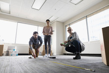 Business People With Tape Measure Measuring Floor Space In New Office