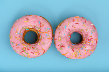 Wall Mural - Sweet pink donuts on a blue background, laid out in the form of eyes, top view. Desserts, game of colors, blue background.