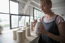 Female Potter Signing, Marking Bottoms Of Clay Vases In Pottery Studio