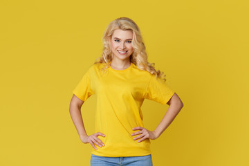 Wall Mural - Photo of a happy young blond woman standing isolated over yellow wall background. Looking at the camera showing the direction of copy space. Banner