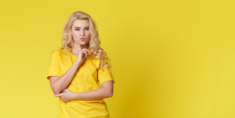 Wall Mural - Photo of a happy young blond woman standing isolated over yellow wall background. Looking at the camera showing the direction of copy space. Banner