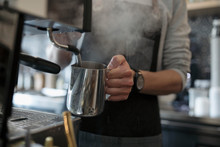 Male Barista Steaming Milk At Espresso Machine In Cafe