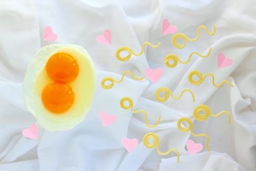 Egg with two yolks and pasta look like sperm competition, Spermatozoons levitate over a background of white sheets with pink hearts. Trendy concept of fertilization, twins, love, Valentine's day.