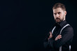 © Kuz Production - Half-turned portrait of masculine bearded man in black shirt and white suspenders isolated black background copyspace