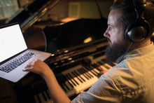 Male Pianist Playing Grand Piano, Writing Music At Laptop In Recording Studio