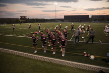 Teenage Girl High School Cheerleading Team Cheering And Jumping On Sideline Of Game On Football Field