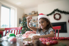 Smiling Girl In Santa Hat Holding Tiny Terrarium Ornament At Table With Christmas Decorations