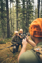 Male Hunter With Camera Phone Photographing Father And Son Hunting In Forest