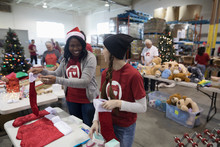 Smiling Female Volunteers In Santa Hat Filling Christmas Stockings In Warehouse