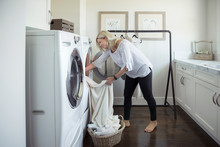 Woman Removing Laundry From Dryer In Laundry Room