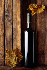 Bottle of red wine and dried vine leaves on a old wooden background.