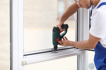 Poster - Construction worker repairing plastic window with electric screwdriver indoors