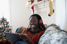 Happy Young Woman With Headphones Watching Movie On Digital Tablet In Christmas Living Room