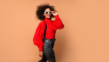 Horizontal Fashion  Image Of Excited Black Woman Jumping With Happy Face Expression On Beige Background. Wearing Vintage Red Shirt