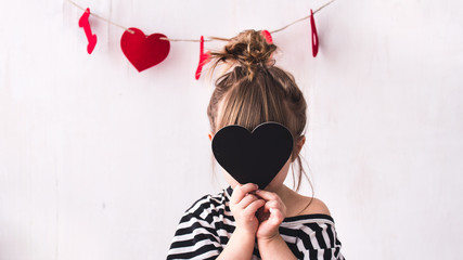 Faceless portrait of a happy kid girl wearing striped t-shirt and playing with card form heart. valentines day, 14 February concept