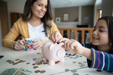 Mother Watching Son Place Coins In Piggy Bank