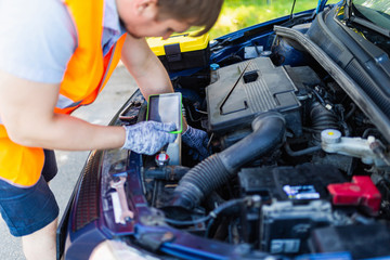 Mechanic in an orange vest with a diagnostic tablet checks the car engine. scheduled maintenance and diagnostics of the car engine. Mechanic With Digital Tablet Showing Graph While Examining Car