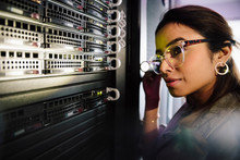 Female IT Technician With Flashlight Examining Equipment In Network Server Room
