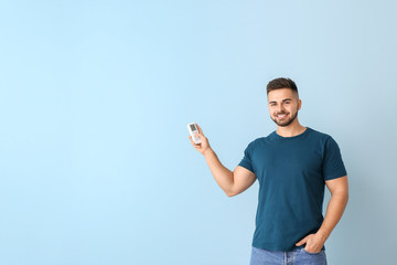 Poster - Young man with air conditioner remote control on color background