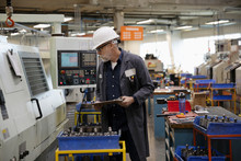 Machine Shop Supervisor Examining Equipment On Factory Floor