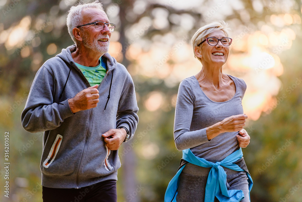 Cheerful active senior couple jogging in the park. Exercise together to stop aging. - obrazy, fototapety, plakaty 