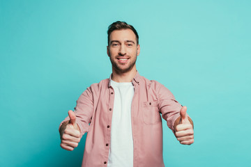 smiling handsome man showing thumbs up, isolated on blue