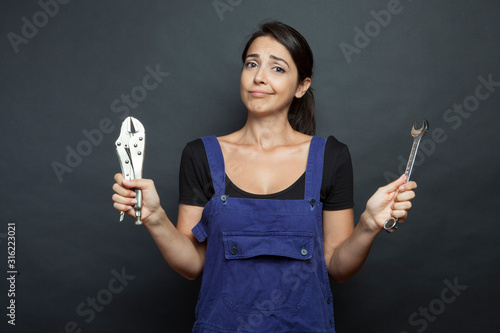 Fotomural ragazza mora vestita con una tuta da meccanico sta con una chiave inglese in man