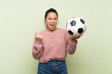 Wall Mural - Young teenager Asian girl over isolated green background holding a soccer ball