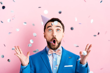 Wall Mural - selective focus of surprised businessman looking at falling confetti on pink