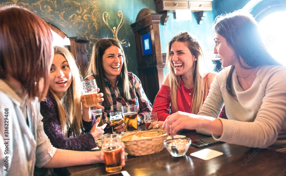 Happy women drinking beer at brewery restaurant - Female friendship concept with young girlfriends enjoying time together and having genuine fun at cool vintage pub - High iso image with soft focus - obrazy, fototapety, plakaty 