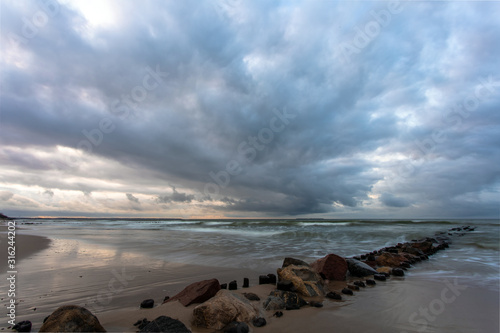 Baltic sea beach with stones and old breakwaters under a gloomy cloudy sky at lo Tableau sur Toile