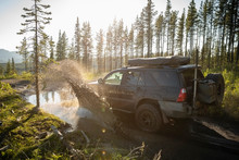SUV Splashing Through Mud On Sunny Remote Road, Overland Adventure, Alberta, Canada