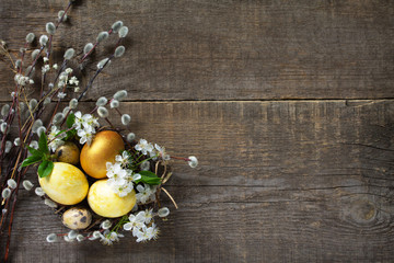 Golden Colored easter eggs in a nest with willow branches and spring flowers on a gray wooden background. Top view flat lay background. Copy spa