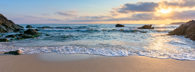 sunrise on the beach. beautiful summer scenery. rocks on the sand. calm waves on the water. clouds on the sky. wide panoramic view