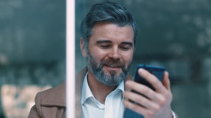 Wall Mural - Portrait of attractive middle aged business man in the café, laughing at the internet memes, jokes. Modern life, being stylish. Texting to a friend. Close up view, slow motion.