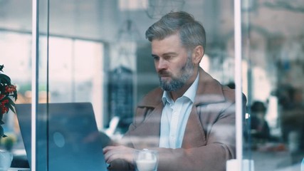 Attractive middle aged businessman sitting working drinking coffee smiling in a cafe. Man using computer devices. Business and entrepreneurship. Successful, confident, social network, apps, laptop.