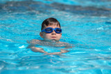 Fototapeta Przestrzenne - European boy in swimming goggles is swimming in the hotel’s pool during his summer vacations.