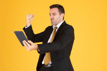 Portrait of cheerful businessman using tablet on yellow  background.