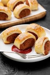 Wall Mural - Delicious homemade sausage rolls served with tomato sauce on a black stone background.