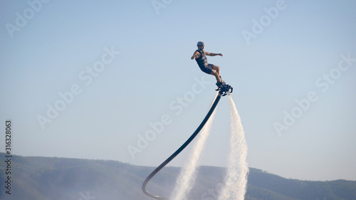 Fotografía extreme athlete is using flyboard on sea, moving legs and torso to control movem