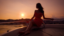 Romantic Young Woman Is Sitting On Board Of Small Pleasure Boat In Sunset Time, Leaning On Handrails